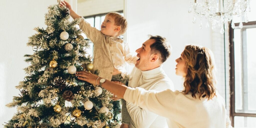 Des parents et leur bébé en train de décorer le sapin de Noël